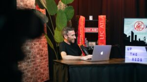 An image of a man smiling while at his laptop on the set of a podcast