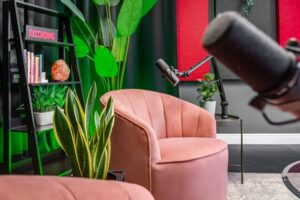 An image of a single seater pink couch surrounding by plants on the set of a podcast